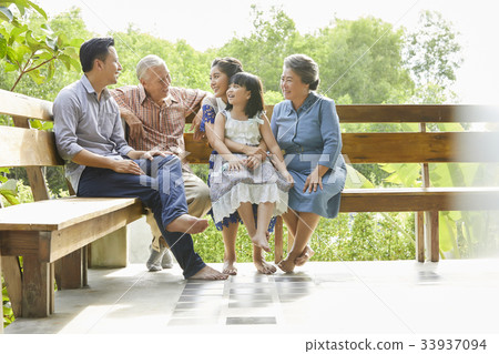 An extended family is sitting, relaxing and having fun on a bench. 33937094