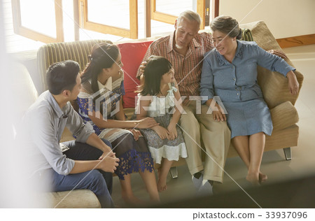 A little girl is sitting beside her parents while the grandparents are looking at her. 33937096