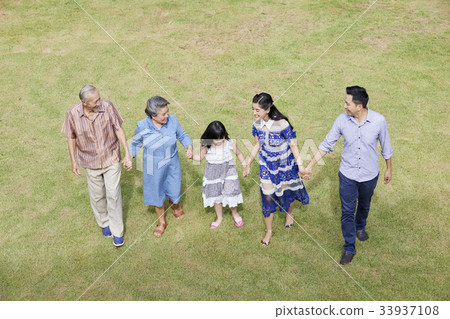 five people in an extended family are holding hands and walking outdoors. 33937108