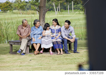 a happy extended family is sitting on a long chair on a sunny day. a happy extended family is sitting on a long chair on a sunny day. 33937109