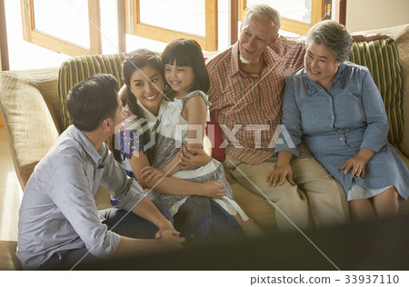 an extended family is sitting on a sofa and having fun together. 33937110