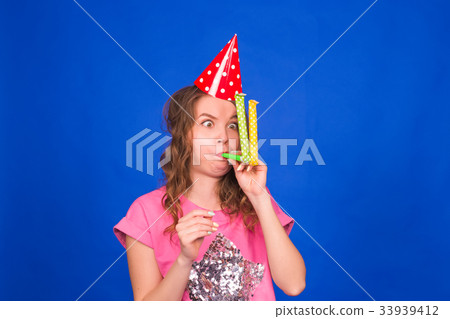 Funny young woman in a birthday cap blowing a Funny young woman in a birthday cap blowing a 33939412