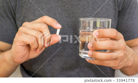 Man holding a pill and a glass of water. 33941778