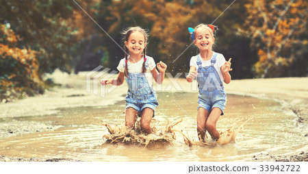 Happy funny sisters twins child girl   jumping on puddles in rubber boots  . 33942722