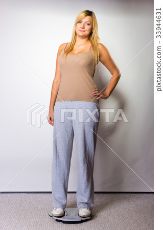 Happy woman wearing tracksuit standing on weighing machine Happy woman wearing tracksuit standing on weighing machine 33944631