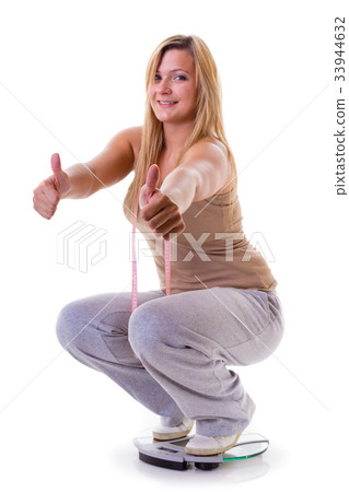 Happy woman wearing tracksuit squating on weighing machine Happy woman wearing tracksuit squating on weighing machine 33944632