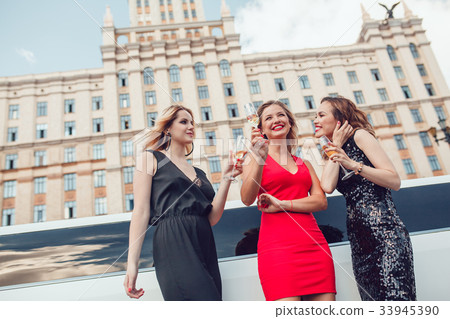 Beautiful women near a limousine drink champagne. Beautiful women near a limousine drink champagne. 33945390