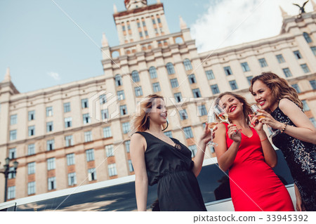 Beautiful women near a limousine drink champagne. Beautiful women near a limousine drink champagne. 33945392