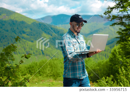 guy smiling and working on laptop in the mountains guy smiling and working on laptop in the mountains 33956715