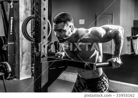 Strong muscular man doing push-ups on uneven bars Strong muscular man doing push-ups on uneven bars 33958162