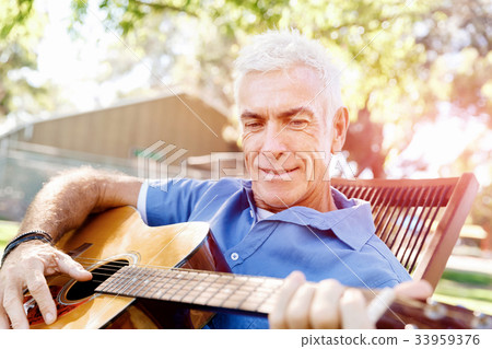 Senior man plying guitar outdoors Senior man plying guitar outdoors 33959376