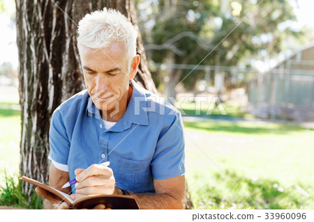 Senior man sittingin park while reading book Senior man sittingin park while reading book 33960096