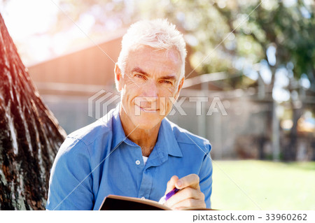 Senior man sittingin park while reading book Senior man sittingin park while reading book 33960262