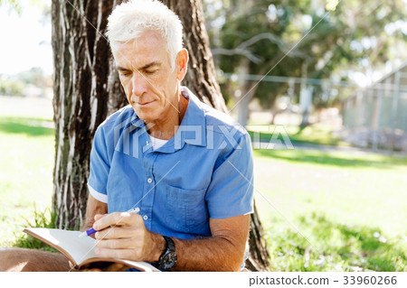 Senior man sittingin park while reading book Senior man sittingin park while reading book 33960266