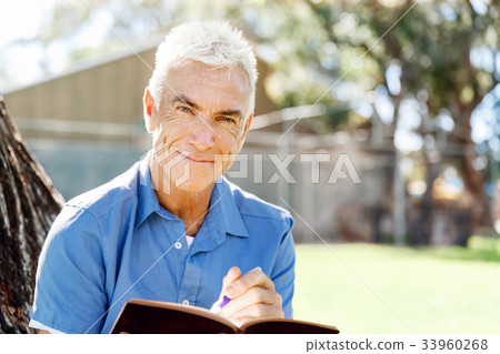 Senior man sittingin park while reading book Senior man sittingin park while reading book 33960268