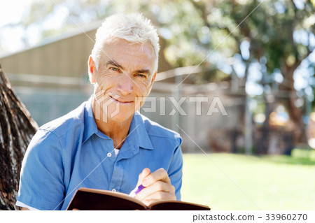 Senior man sittingin park while reading book Senior man sittingin park while reading book 33960270