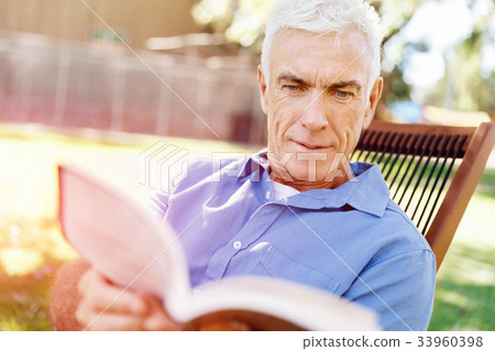 Senior man sittingin park while reading book Senior man sittingin park while reading book 33960398