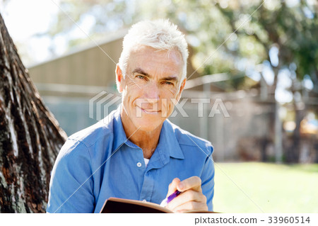 Senior man sittingin park while reading book Senior man sittingin park while reading book 33960514