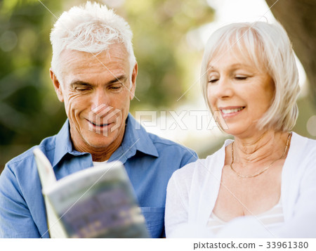 Nice elderly couple sitting outdoors with book Nice elderly couple sitting outdoors with book 33961380
