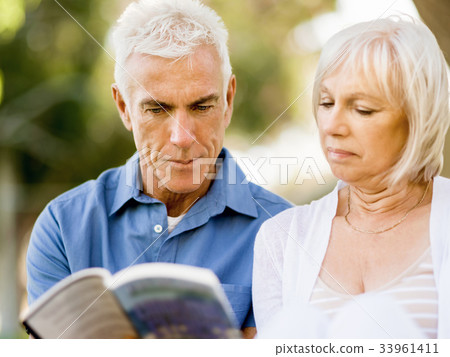 Nice elderly couple sitting outdoors with book Nice elderly couple sitting outdoors with book 33961411