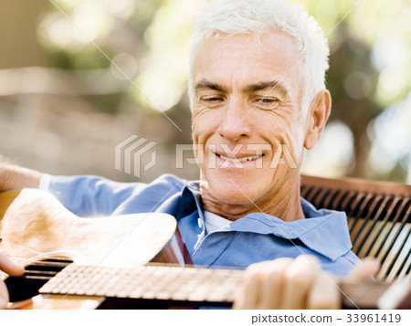 Senior man plying guitar outdoors Senior man plying guitar outdoors 33961419