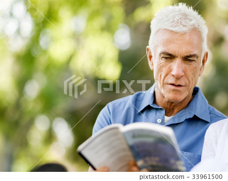 Senior man sittingin park while reading book 33961500