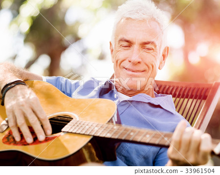 Senior man plying guitar outdoors 33961504