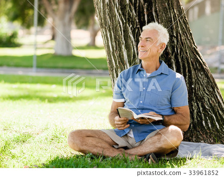 Senior man sittingin park while reading book Senior man sittingin park while reading book 33961852