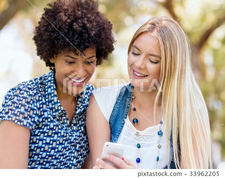 Two women friends in park with mobile phone 33962205