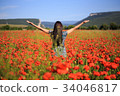 Woman stands with open arms on summer poppy field 34046817