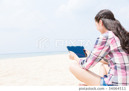 Woman using tablet on sandy beach Woman using tablet on sandy beach 34064511