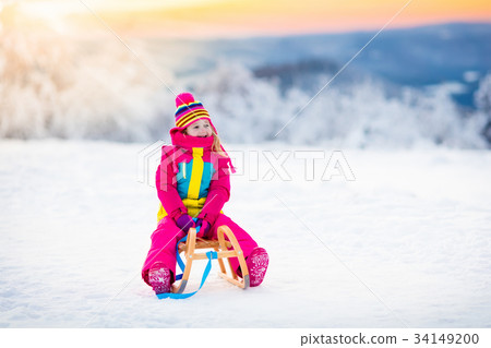 Child playing in snow on sleigh in winter park 34149200
