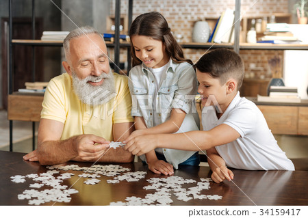 Siblings and their grandfather assembling a jigsaw 34159417