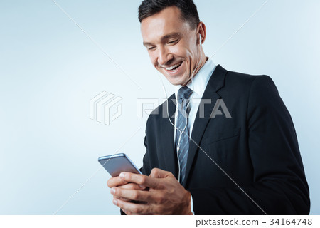 Cheerful joyful man using his smartphone Cheerful joyful man using his smartphone 34164748