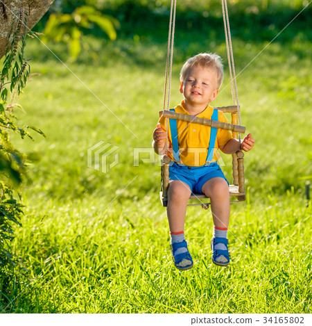 Rural scene with toddler boy swinging outdoors. 34165802