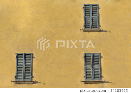 Closed green windows on yellow wall of old house Closed green windows on yellow wall of old house 34185925