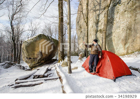Male hiker nearly his red tent in the mountains Male hiker nearly his red tent in the mountains 34198929