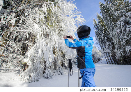 Rear view of skier taking picture with her cell phone Rear view of skier taking picture with her cell phone 34199325