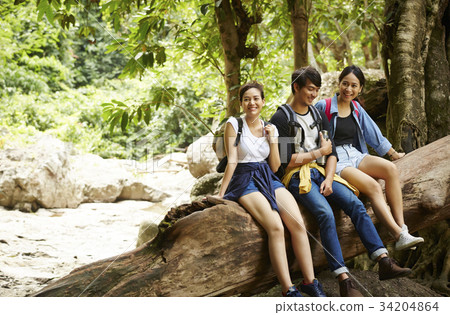 a man and his friends are sitting on the trunk in the forest. 34204864