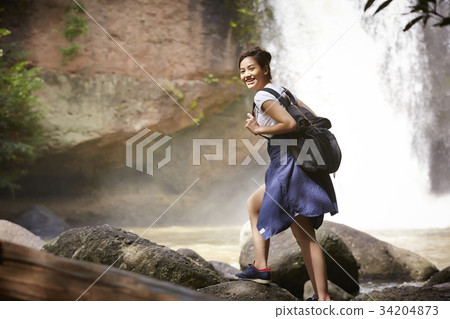 A happy traveler is walking on the rock near the waterfall. 34204873