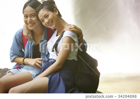 two female hikers are sitting side by side and arm in arm in the forest. two female hikers are sitting side by side and arm in arm in the forest. 34204898