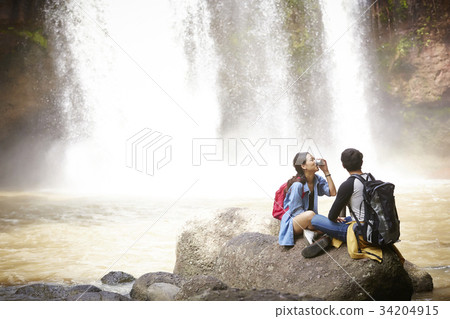 A woman is drinking water with her boyfriend near the waterfall. 34204915