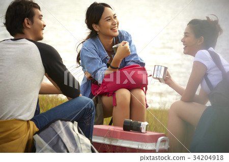 Three young people are talking and resting together on the riverside. 34204918