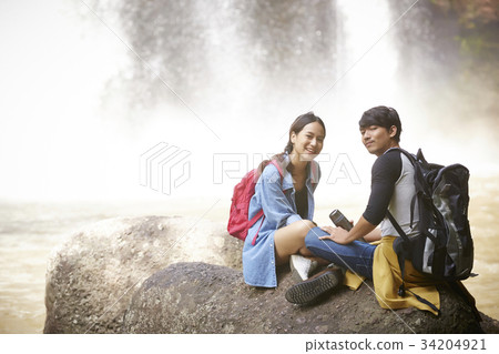 A couple is sitting on the rock to relax near the waterfall. 34204921