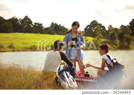 young travelers are relaxing together at sunset on the riverside 34204945
