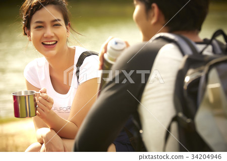 two young friends are having fun and drinking together near the river. 34204946