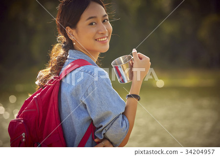 A happy young woman is posing with a cup and drinking beside the river A happy young woman is posing with a cup and drinking beside the river 34204957