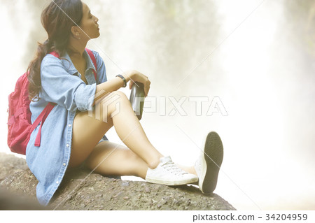 young girl is sitting on the rock and enjoying a waterfall view 34204959