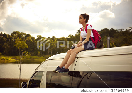 A girl is resting on the rooftop of the van near a river in the forest 34204989