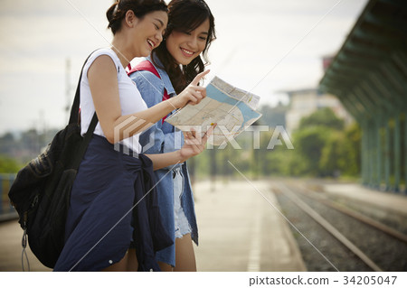 two happy young girls are standing and looking map near a railway 34205047